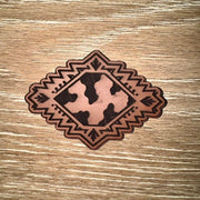 Cow print Aztec diamond laser-engraved leather-look iron-on patch with geometric southwestern border by On A Whim Hats
