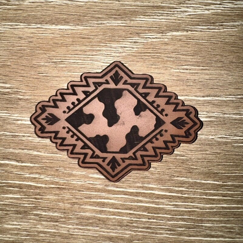 Cow print Aztec diamond laser-engraved leather-look iron-on patch with geometric southwestern border by On A Whim Hats