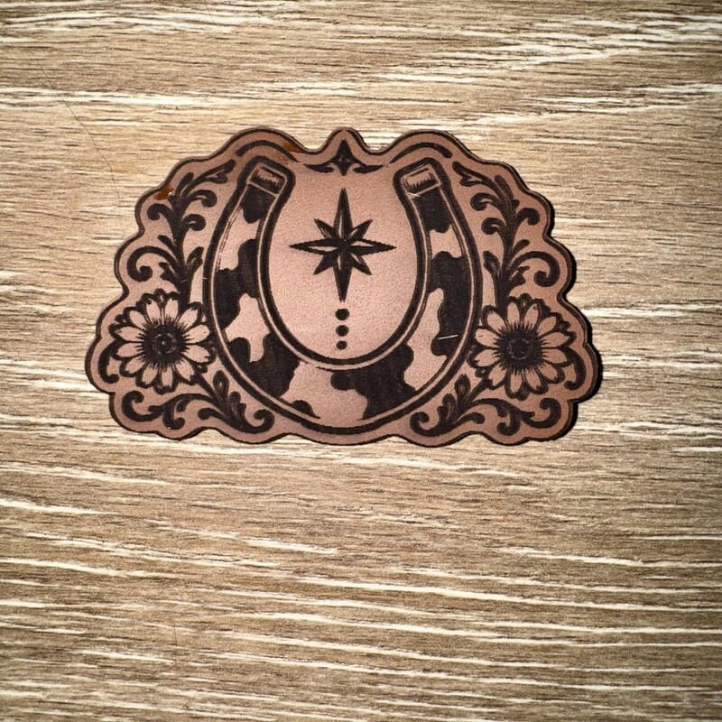 Cow print horseshoe and sunflowers laser-engraved leather-look iron-on patch with north star and scrollwork by On A Whim Hats