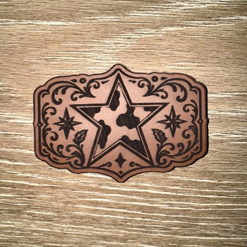 Cow print western star laser-engraved leather-look iron-on patch in a floral buckle-style frame by On A Whim Hats