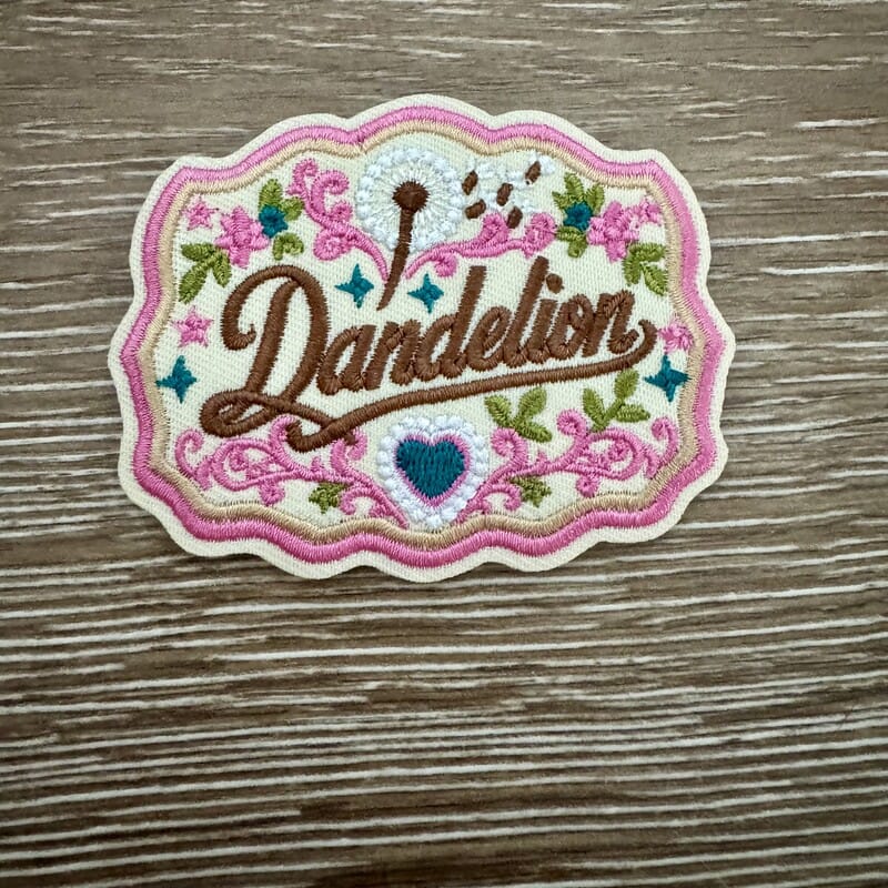 Dandelion floral frame embroidered iron-on patch with pink scrollwork, wildflowers and blue heart