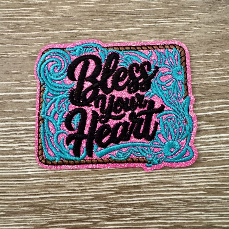 Bless Your Heart western glitter iron-on patch with black script, pink glitter base and teal floral embroidery