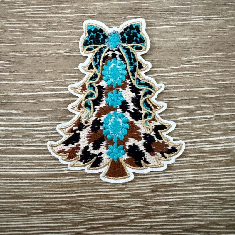 Cow print Christmas tree iron-on patch with turquoise floral medallions and a sparkly bow topper by On A Whim Hats