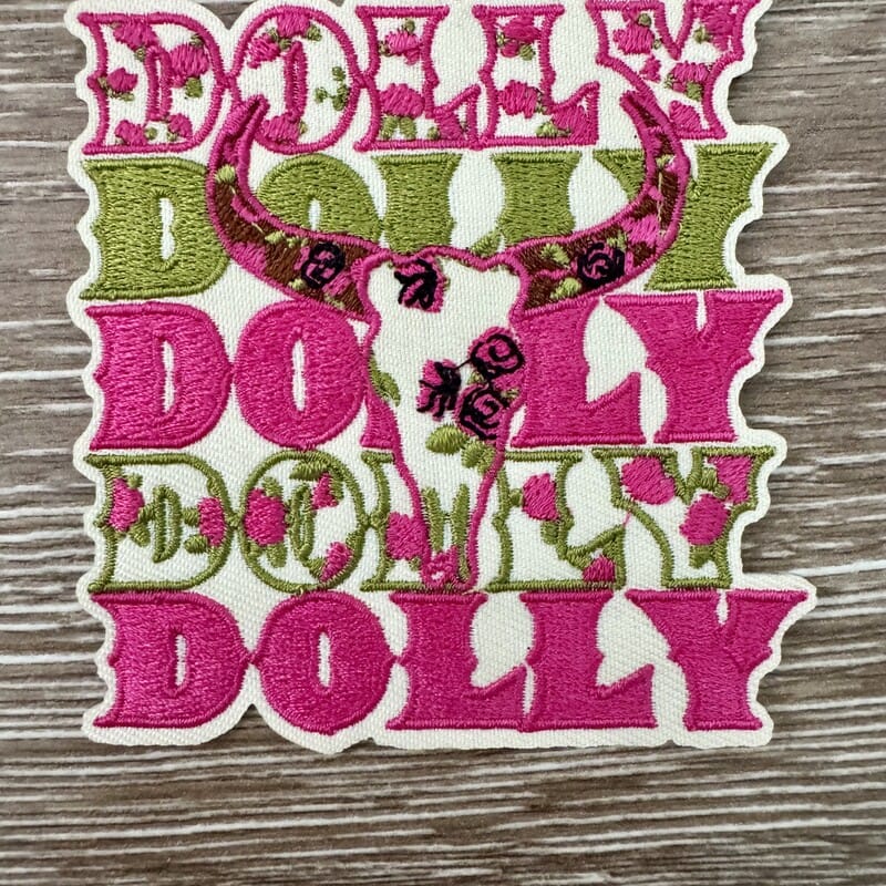 Dolly Country Icon iron-on patch with a floral cattle skull over repeated pink and green lettering by On A Whim Hats