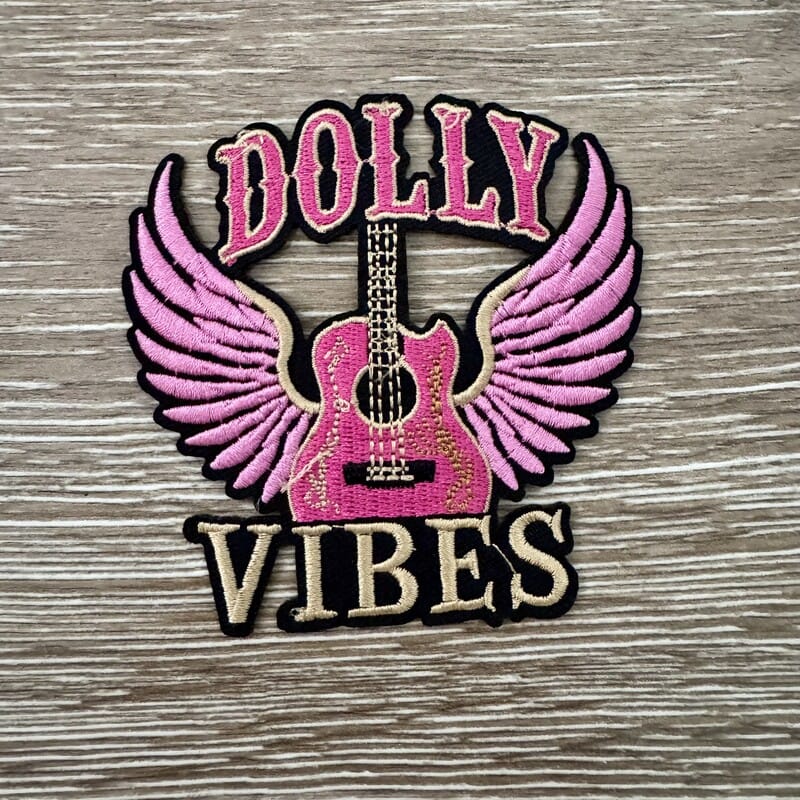 Dolly Country Vibes iron-on patch with a pink acoustic guitar with angel wings and bold lettering by On A Whim Hats