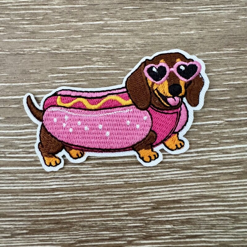 Hot Dog Doxie iron-on patch of a dachshund in a pink bun costume with mustard and heart sunglasses by On A Whim Hats