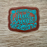 Well Sheeyit western faux-leather iron-on patch with teal cursive script, floral scrollwork and bow details by On A Whim Hats