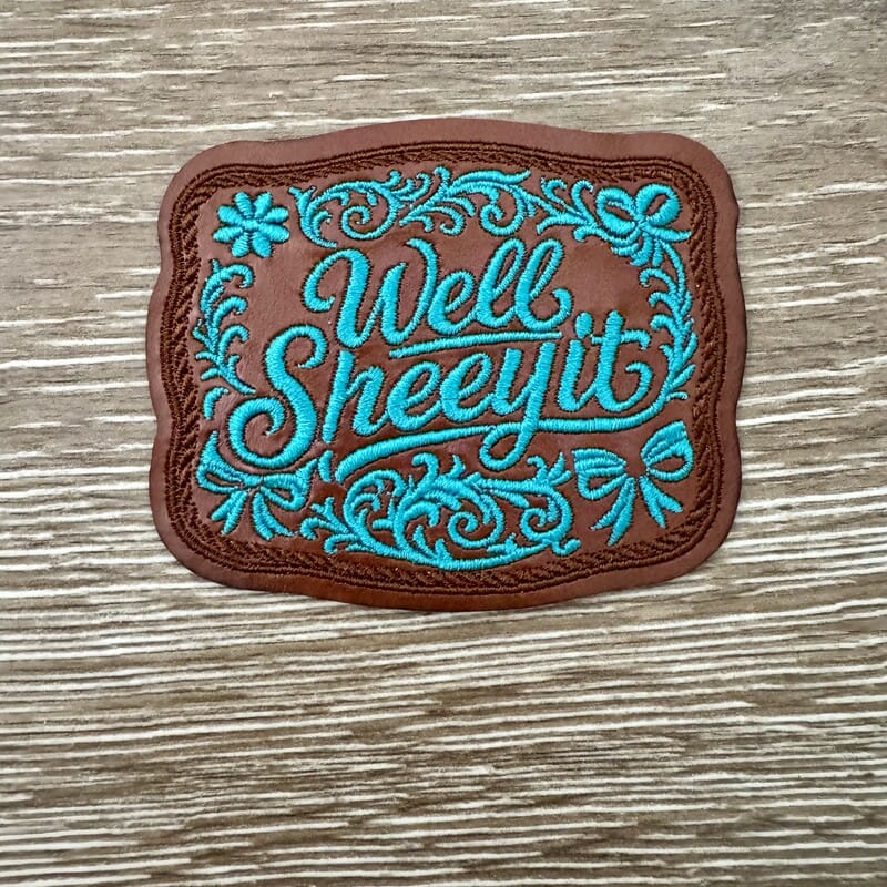 Well Sheeyit western faux-leather iron-on patch with teal cursive script, floral scrollwork and bow details by On A Whim Hats