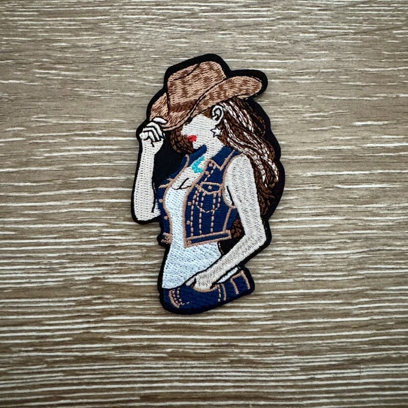 Denim cowgirl pinup iron-on patch with hat-tipping cowgirl in denim vest and red bandana