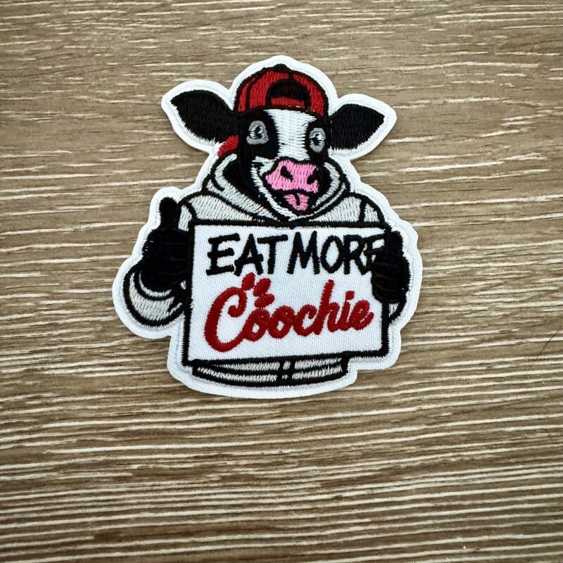 Eat More funny cow sign iron-on patch with smirking cow in backwards cap holding hand-lettered sign