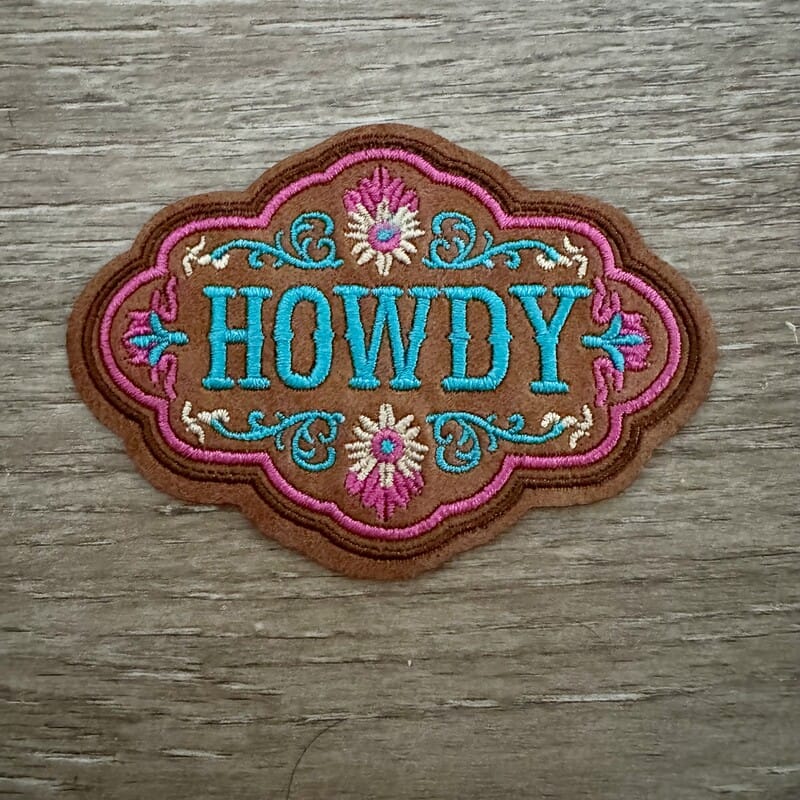 Howdy floral leather iron-on patch with turquoise lettering, pink scalloped border and folk flowers