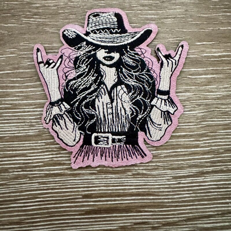 Rock On Cowgirl iron-on patch with wild-haired cowgirl throwing rock hands in black on pink