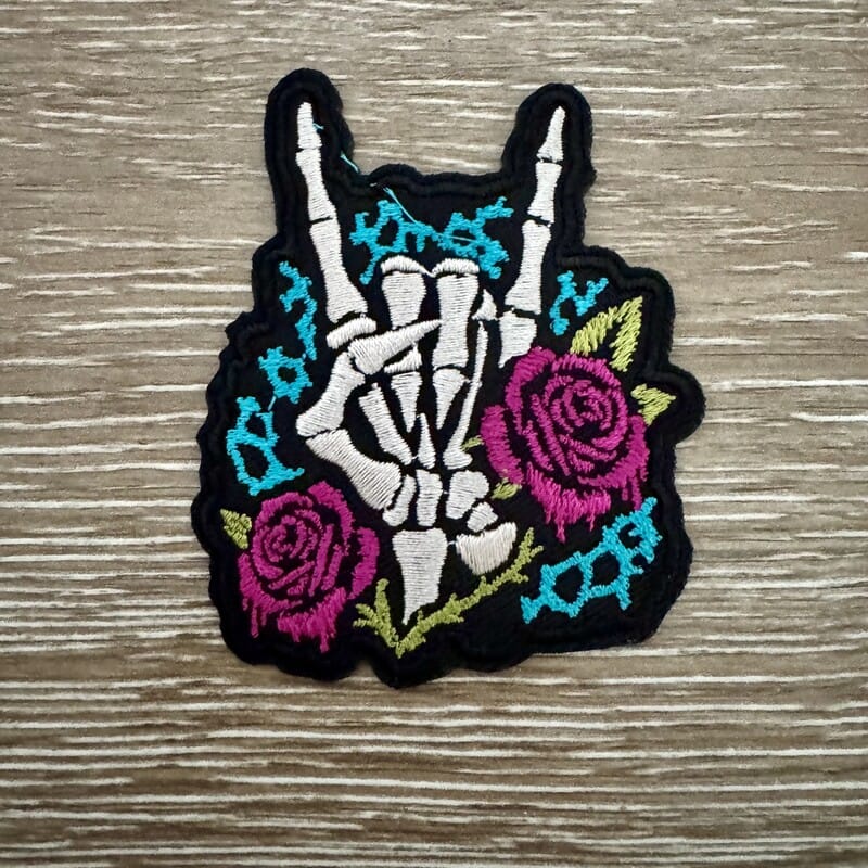 Rock On skeleton hand iron-on patch with magenta roses and teal barbed wire on black