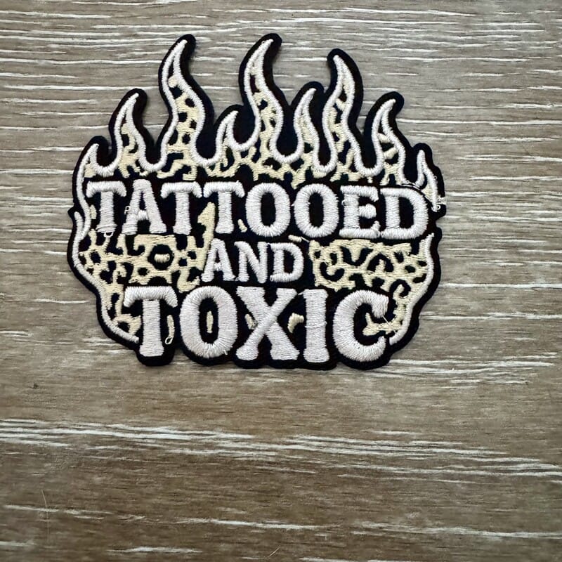 Tattooed and Toxic flame-shaped iron-on patch with leopard lettering